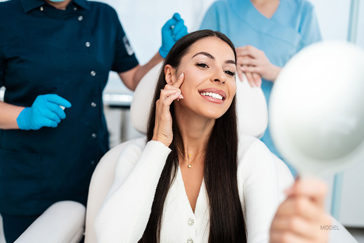 Woman sits in medical office looking in a mirror and smiling